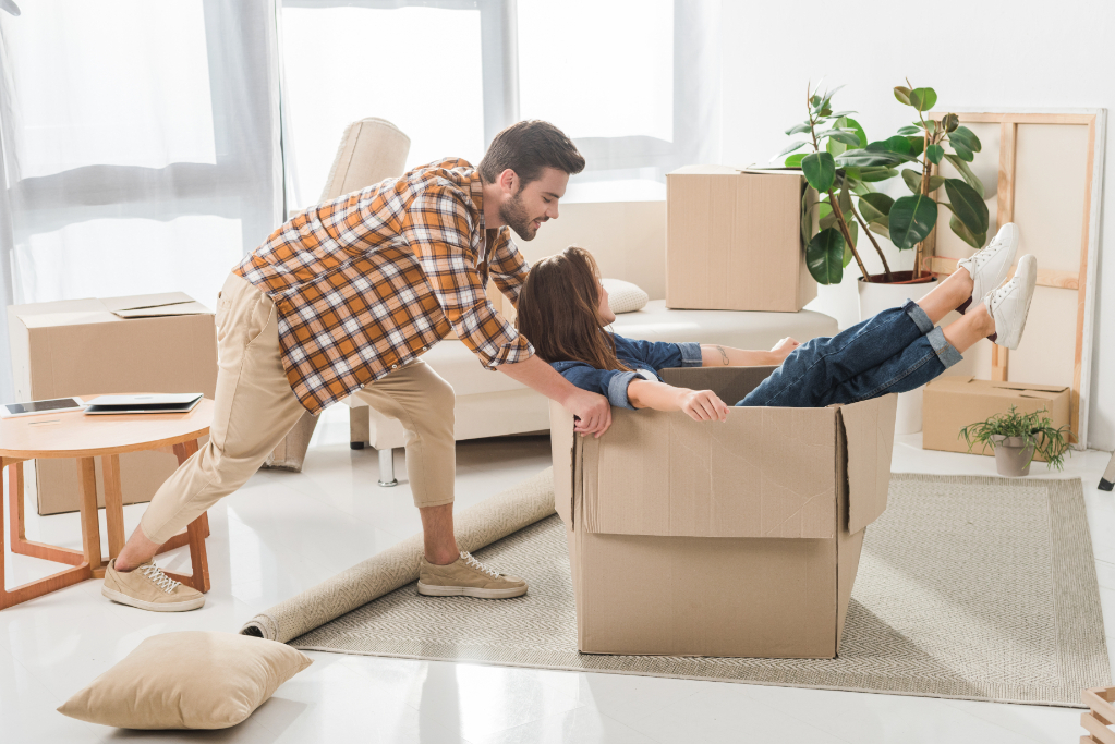 Side view of couple having fun with cardboard box at new house, moving home concept